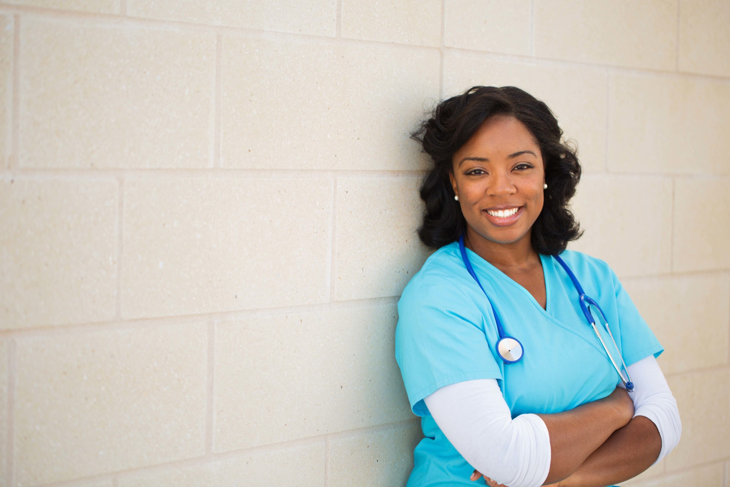 Healthcare provider smiling at the camera with arms crossed on a beige background