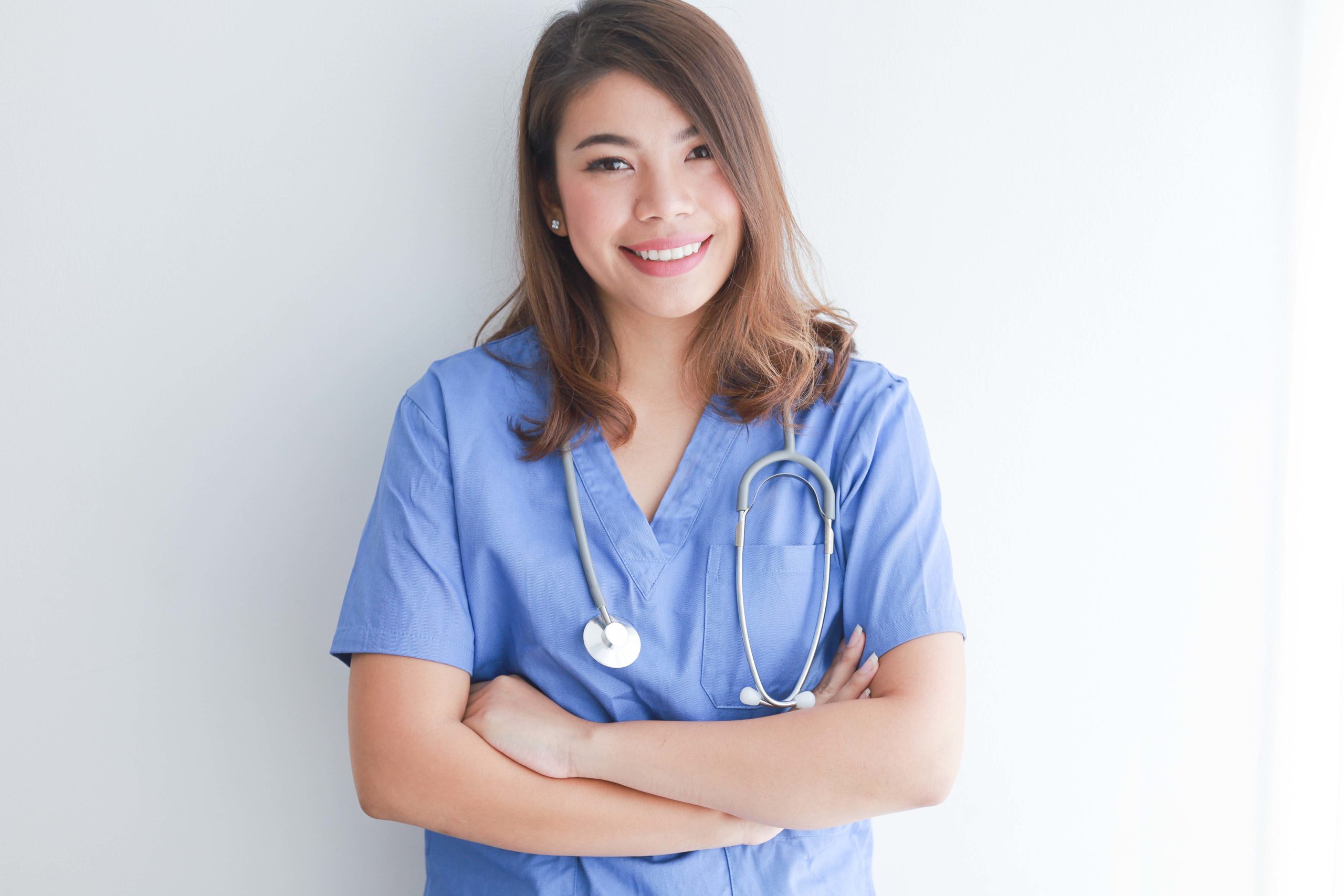 Young nurse in blue scrubs with arms crossed smiling at camera